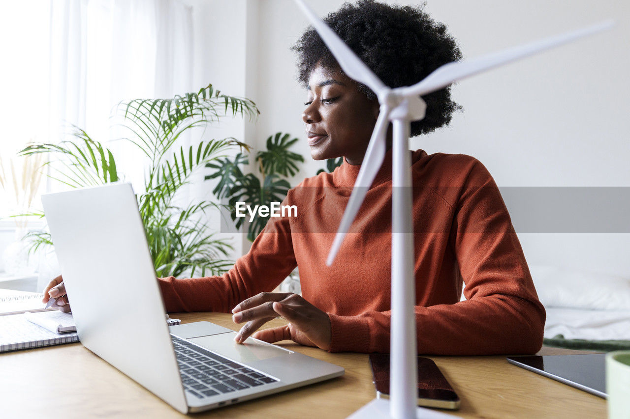 Smiling businesswoman sitting with laptop and wind turbine model at desk