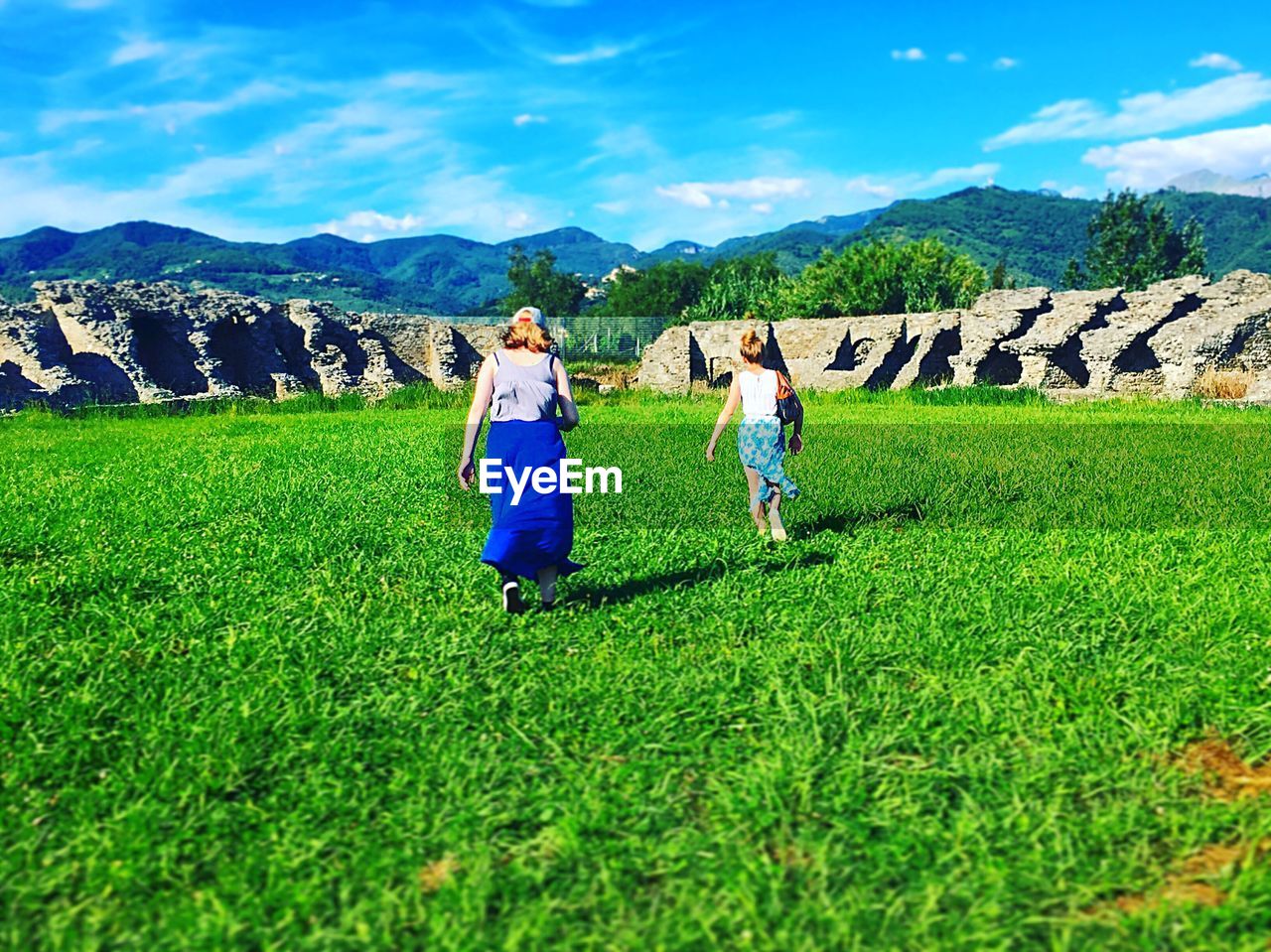 REAR VIEW OF COUPLE ON FIELD AGAINST MOUNTAIN