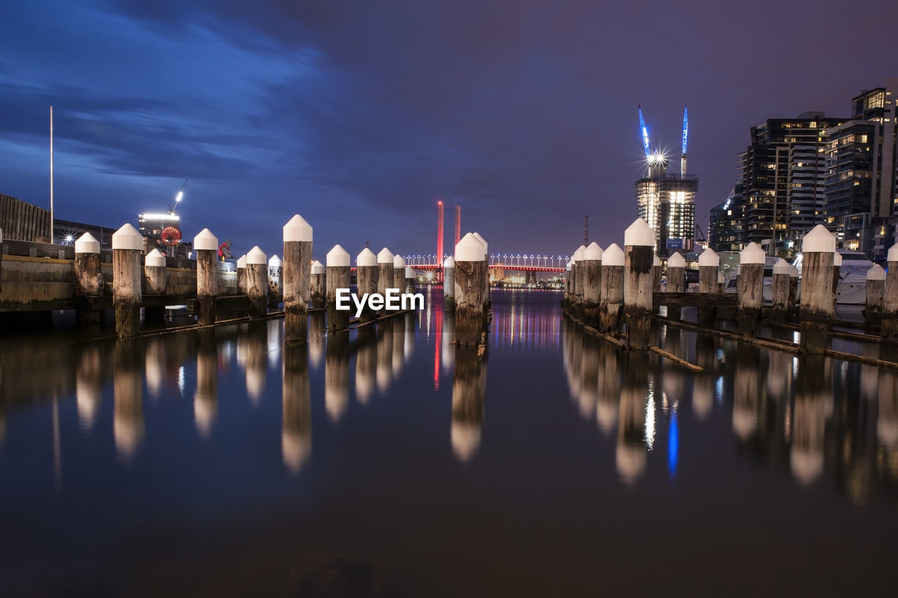 Wooden posts on river against sky in city at night