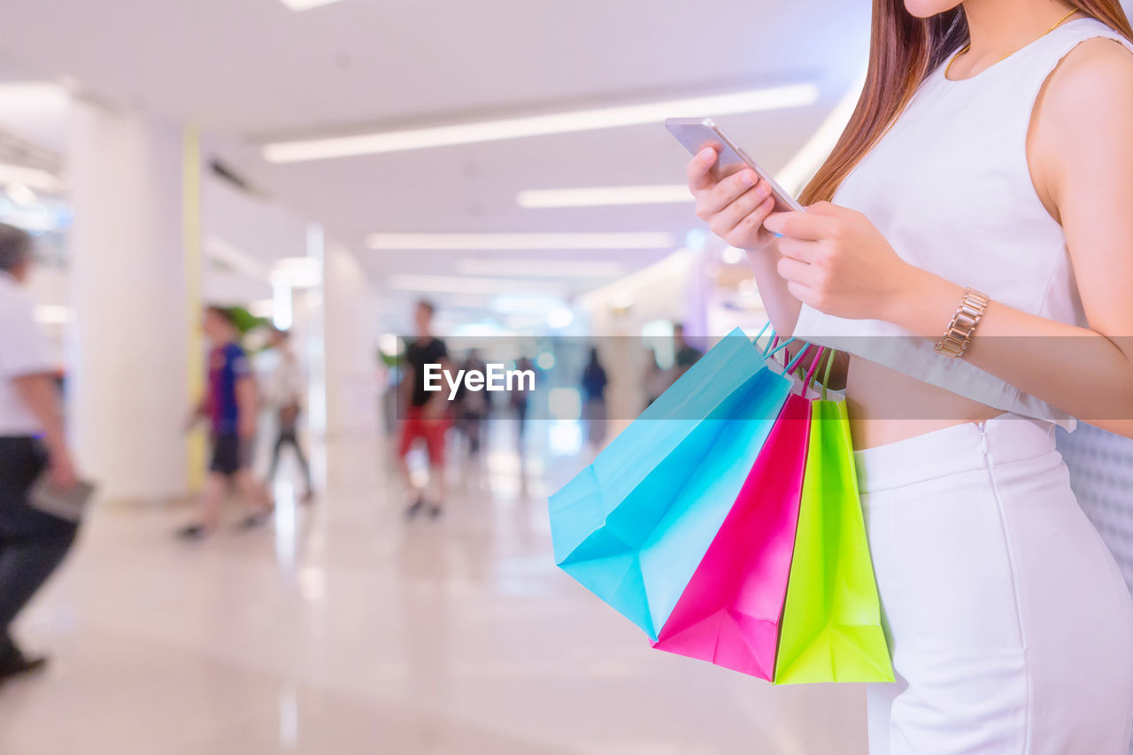 MIDSECTION OF WOMAN WITH UMBRELLA AT SHOPPING MALL