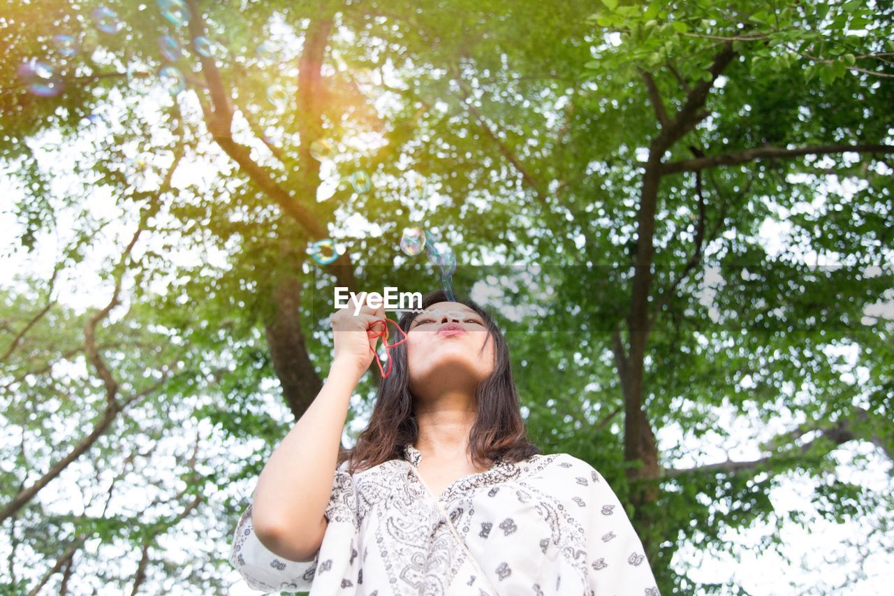 Low angle view of woman blowing bubbles against trees