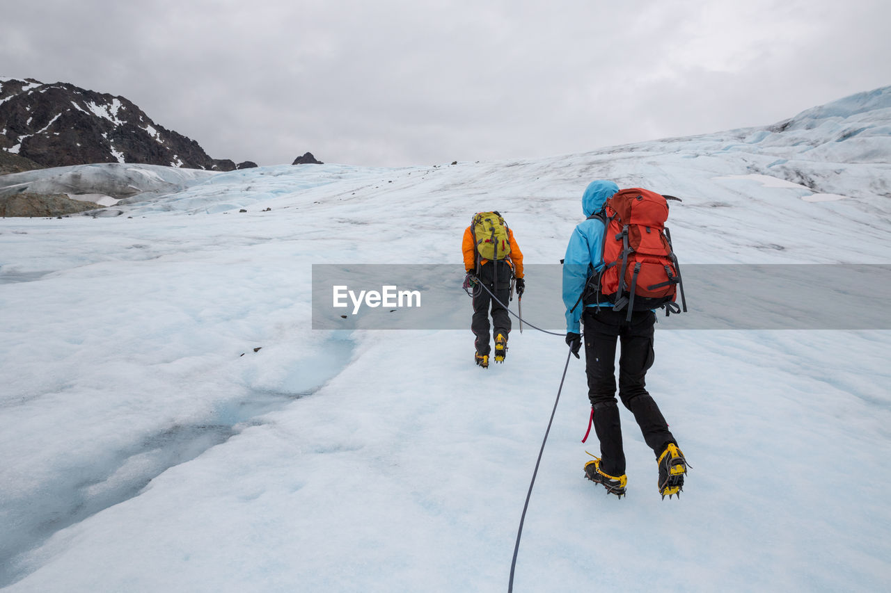 Rear view of people hiking on snow covered mountains against cloudy sky