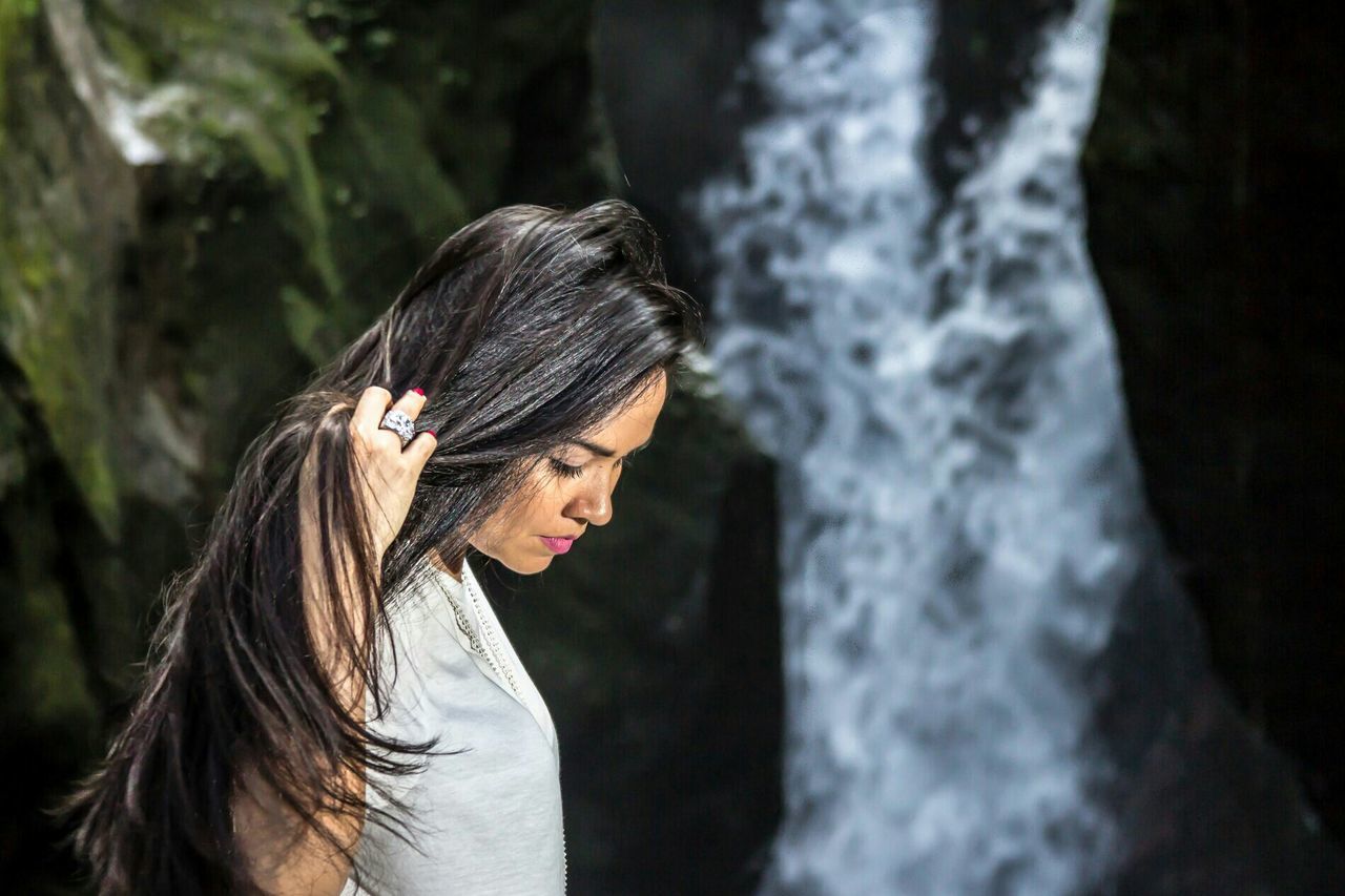 Beautiful woman with hand in hair against waterfall at forest