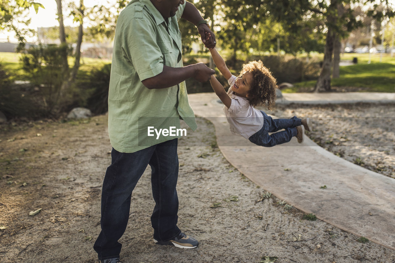 Midsection of playful father swinging son while playing at park