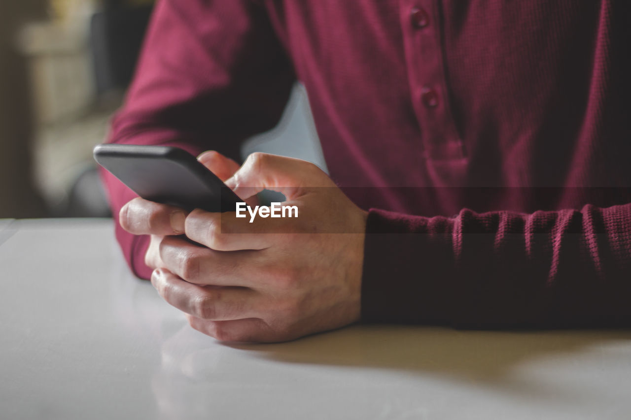 Midsection of man using mobile phone at table