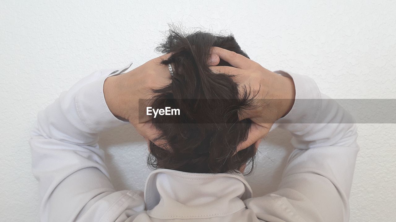 Rear view of woman with hands in hair towards wall at home