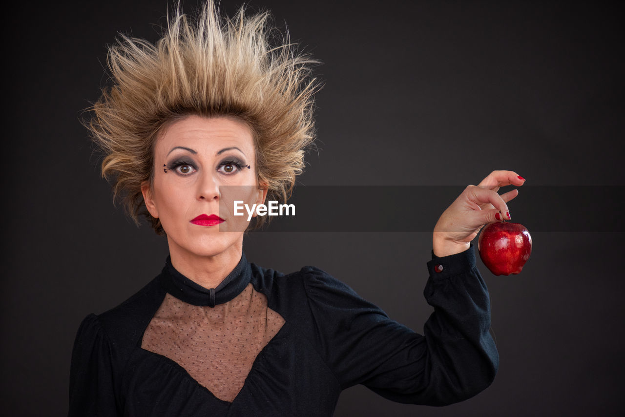 Portrait of woman with crazy hair holding a apple against black background