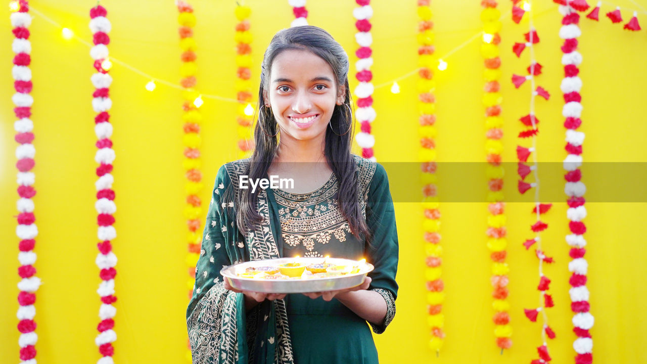 Young girl holding diwali oil diya on her hand in fairy light background and smiling from the heart.