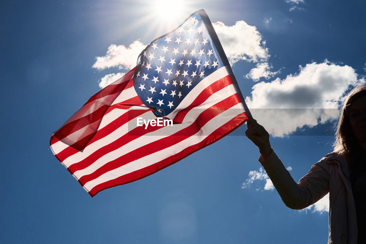 American flag outdoors. woman silhouette holds usa national flag against blue cloudy sky