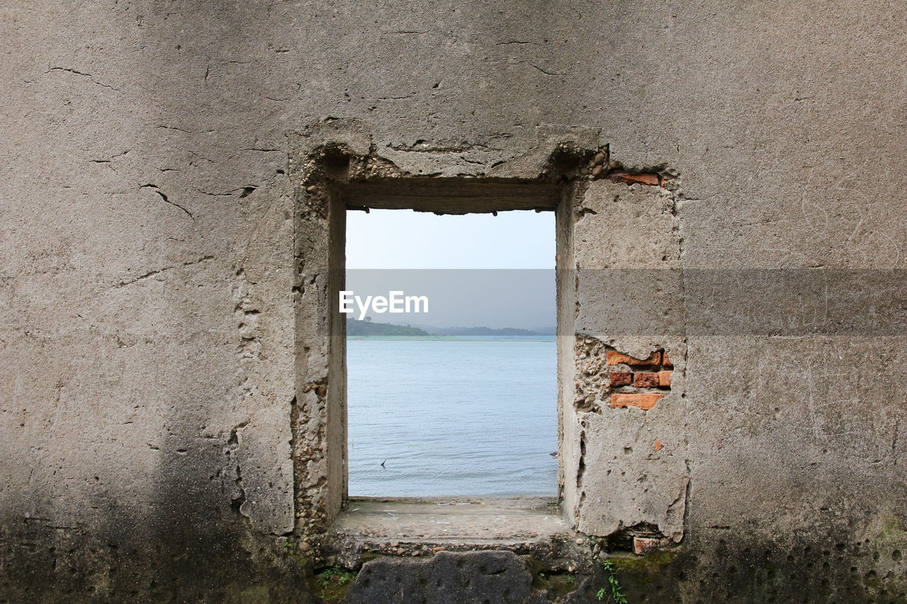 Window of old building by sea against sky