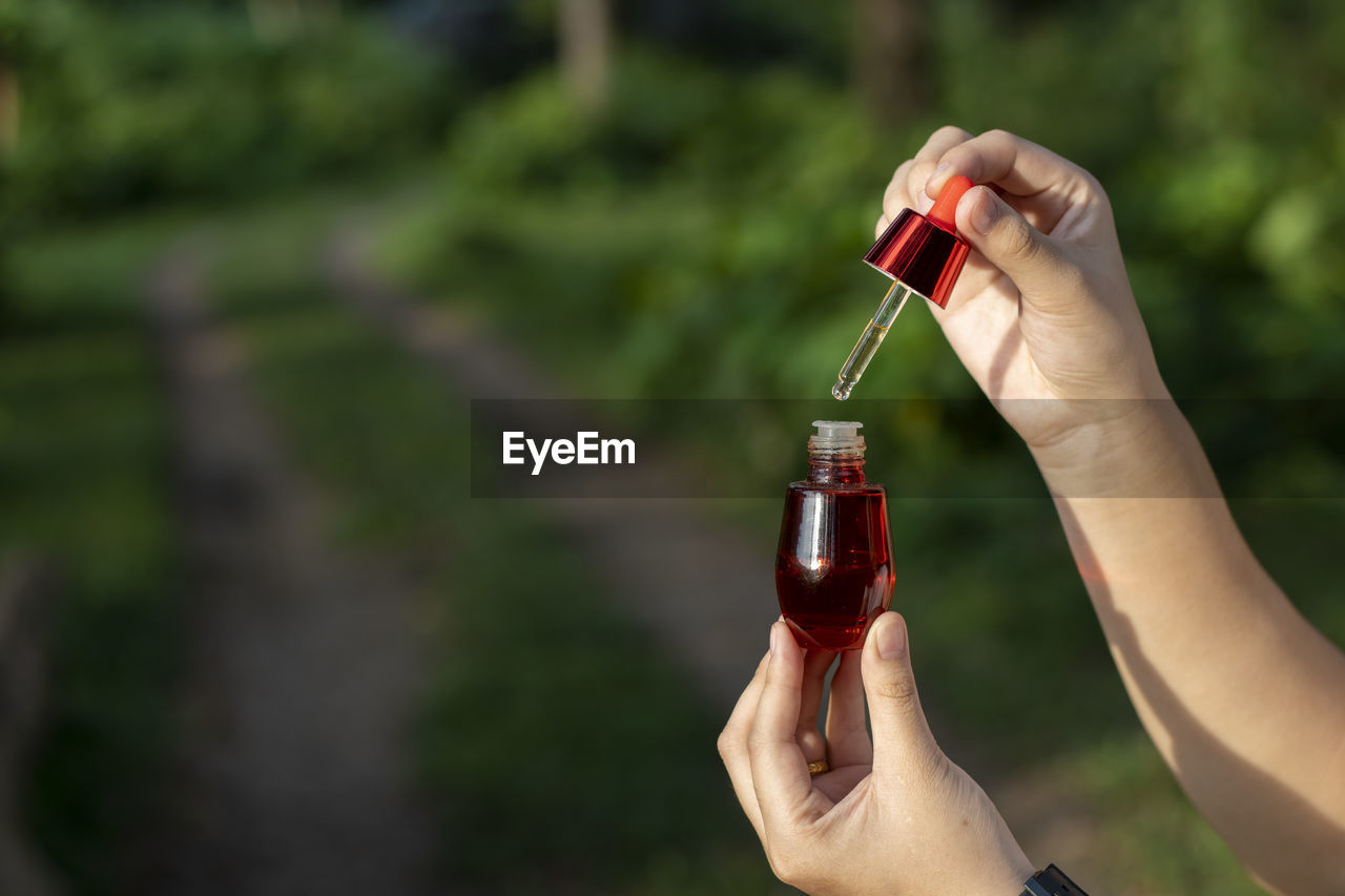 Selective focus red facial serum bottle in asian woman's hand nature background 