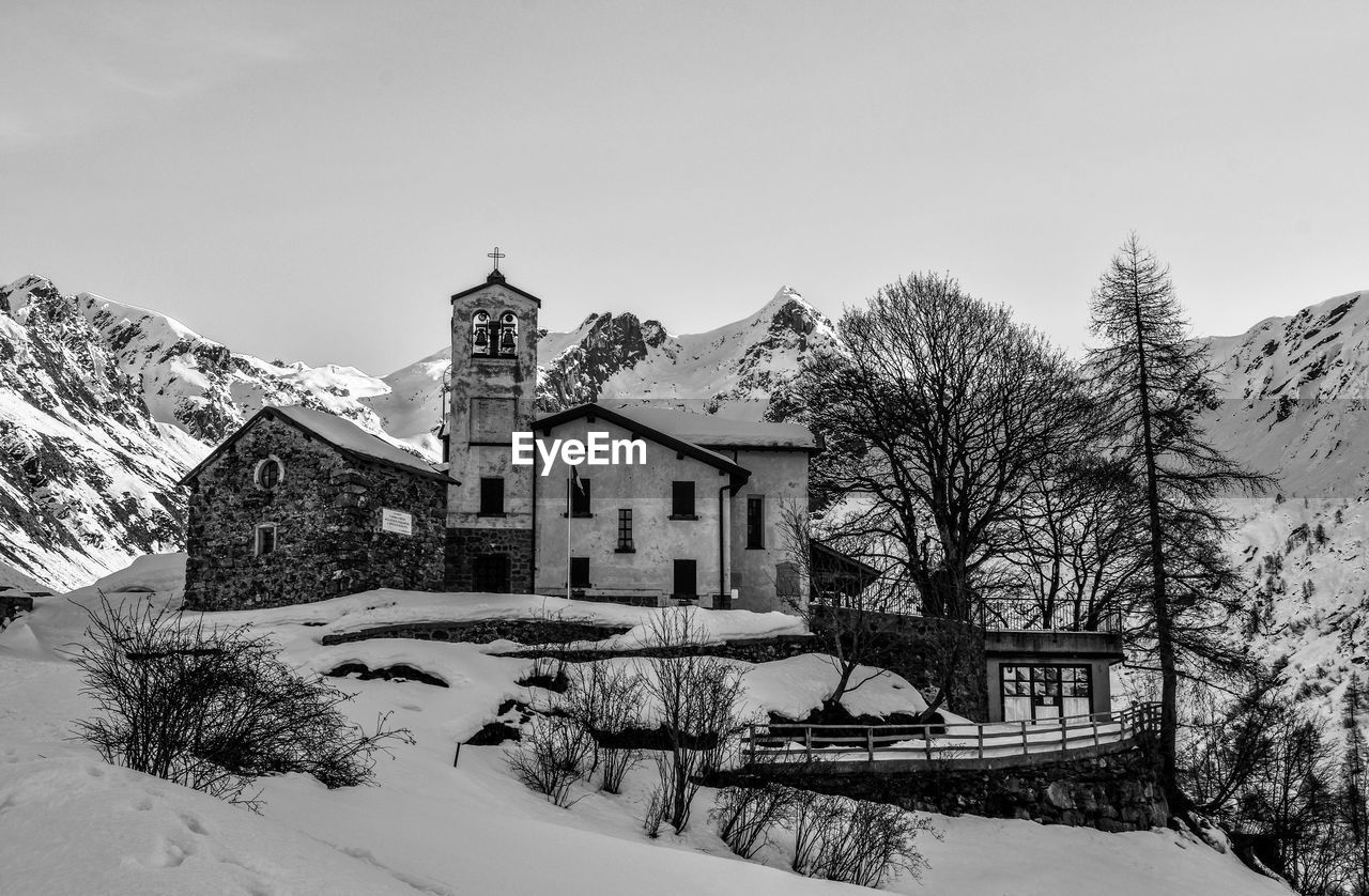 HOUSES BY SNOW COVERED TREES AGAINST SKY