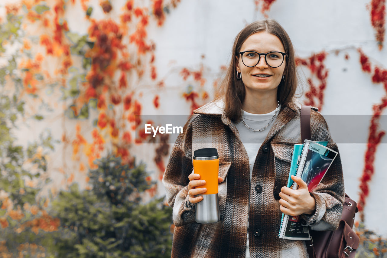 PORTRAIT OF SMILING WOMAN STANDING AGAINST DRINK