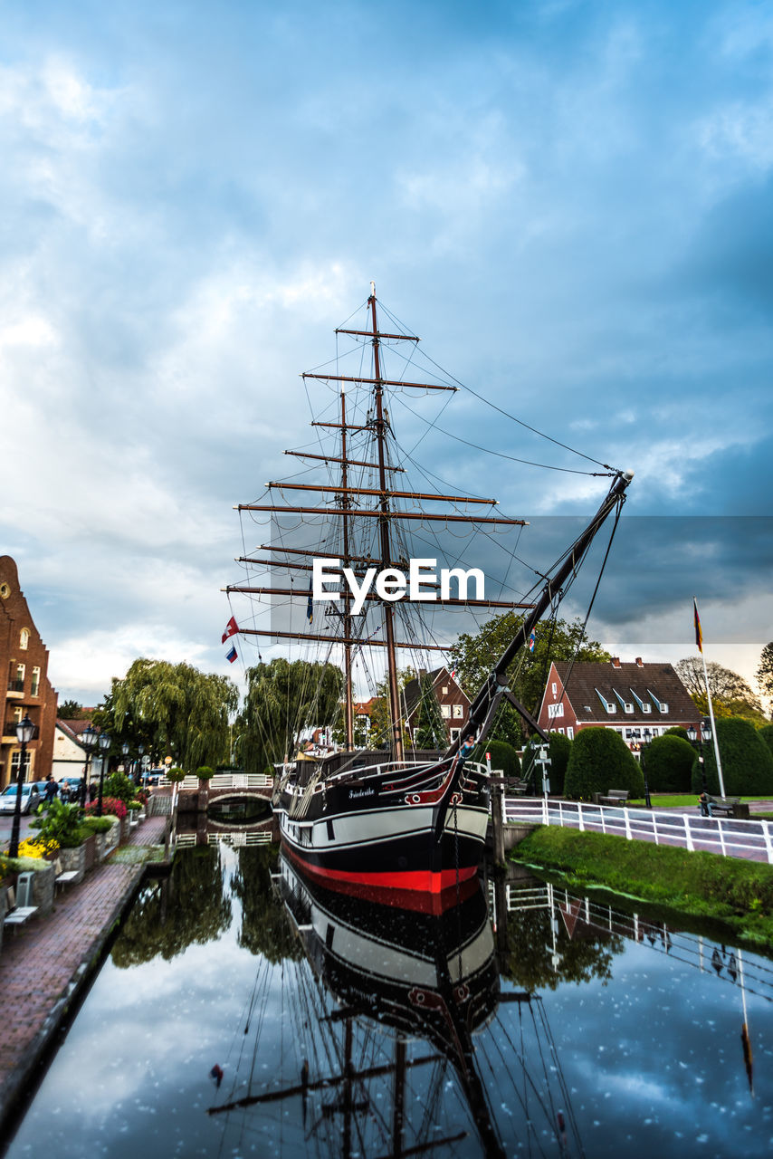 Sailboats moored on canal in city against sky