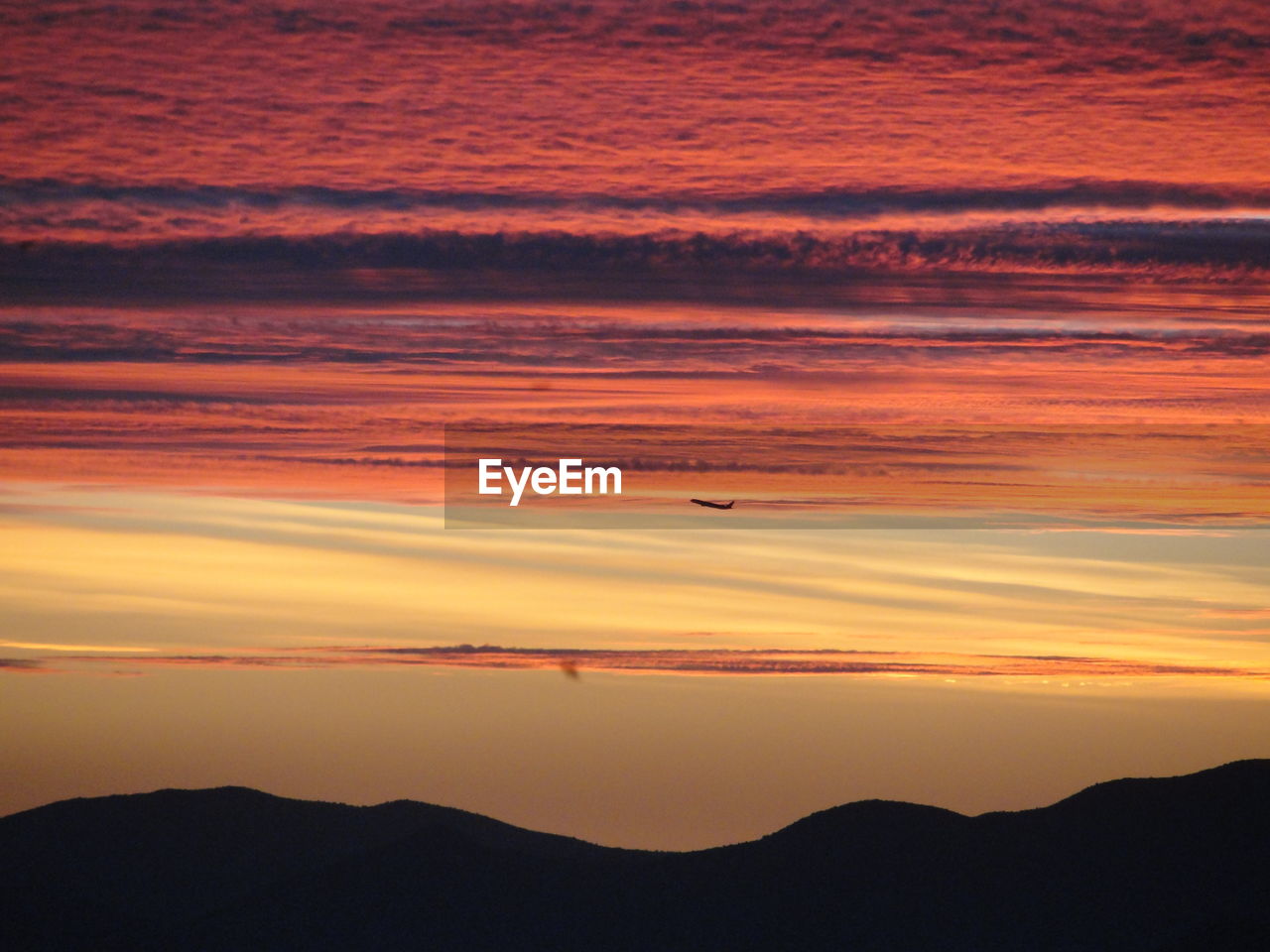 Airplane flying in sky over mountains during sunset