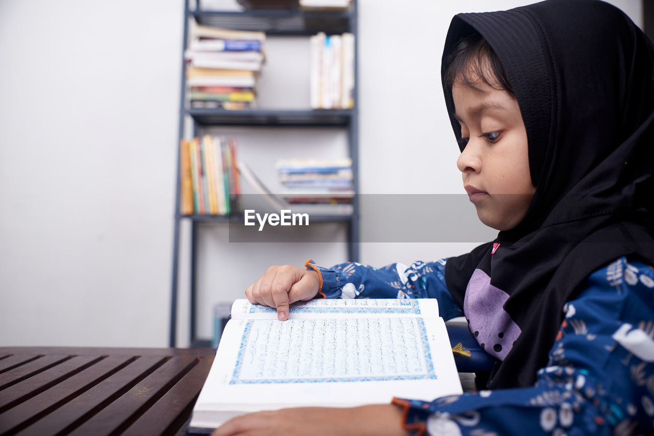 Asian little girl reading koran after praying at home