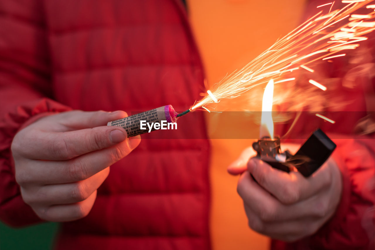 CROPPED IMAGE OF MAN HOLDING SPARKLER AGAINST FIRE