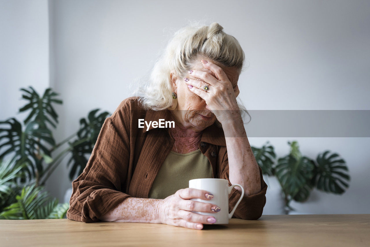 Depressed senior woman with mug on table at home