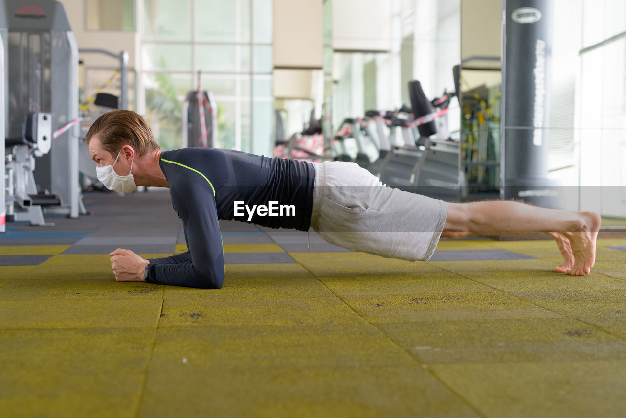 Side view of man wearing mask exercising in gym