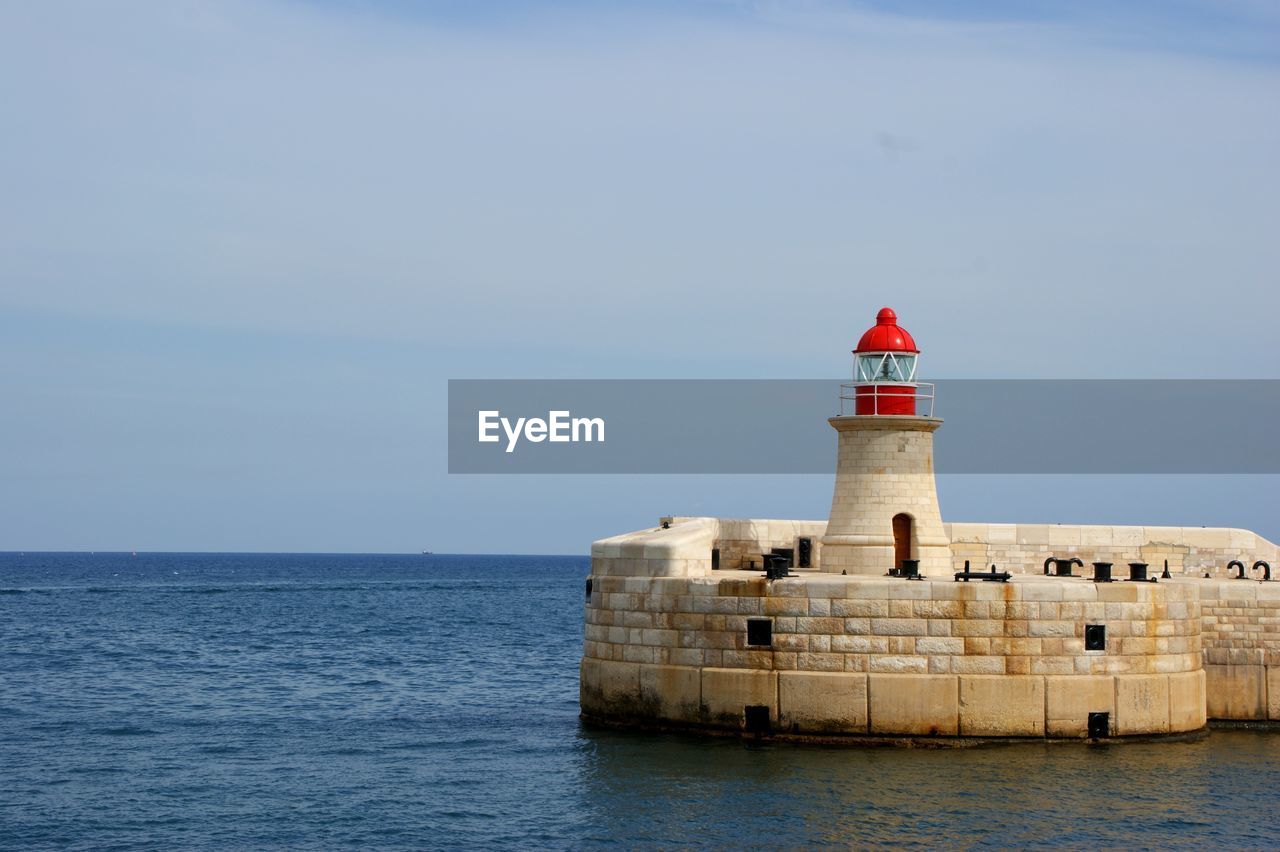 LIGHTHOUSE BY SEA AGAINST SKY AND BUILDING AGAINST CLEAR BLUE TOWER