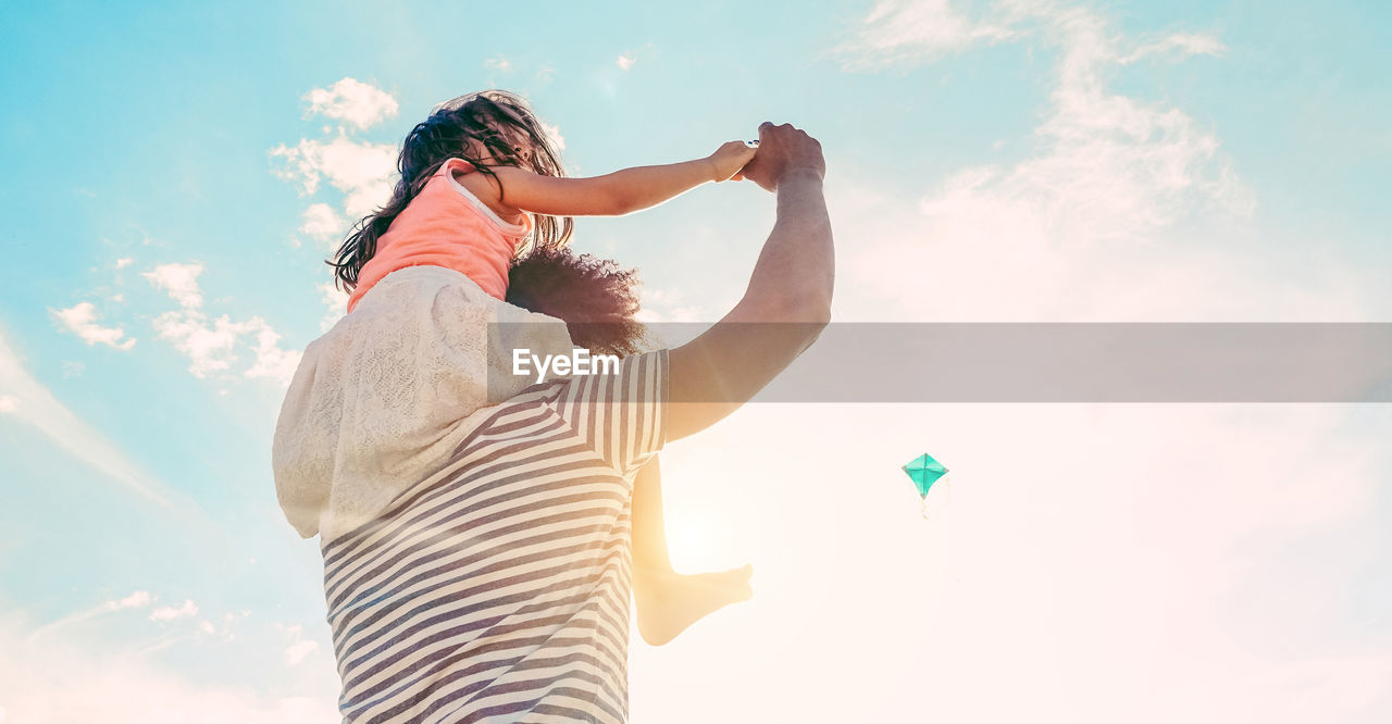 Father carrying daughter on shoulders against sky