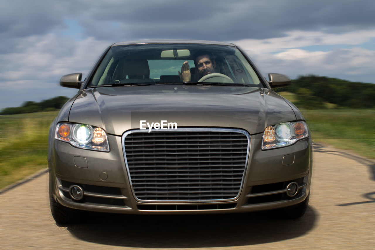 Angry man gesturing in car seen through windshield against cloudy sky