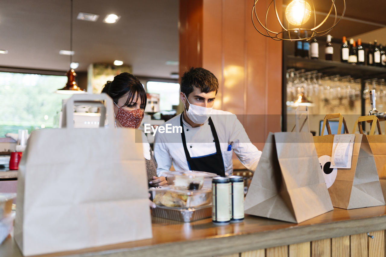 Female owner and male chef checking take out food orders on bar counter during pandemic