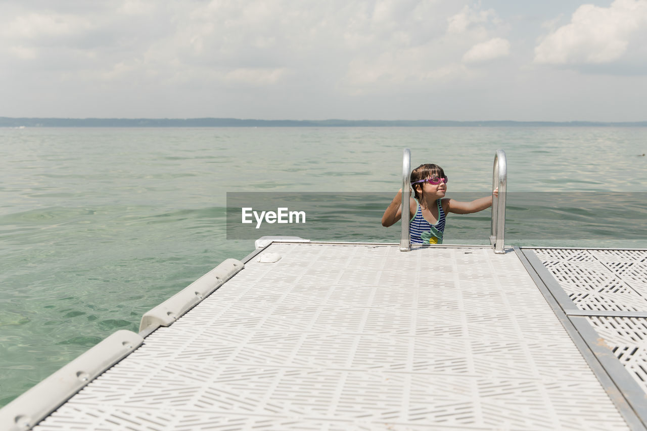 Cute brunette girl with goggles climbs out of lake michigan onto dock