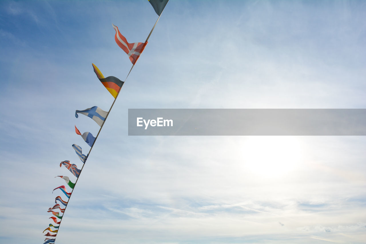 sky, windsports, kite sports, nature, cloud, toy, sports, kite - toy, kite, environment, wind, flying, blue, low angle view, flag, multi colored, day, sunlight, outdoors, no people, beauty in nature, copy space