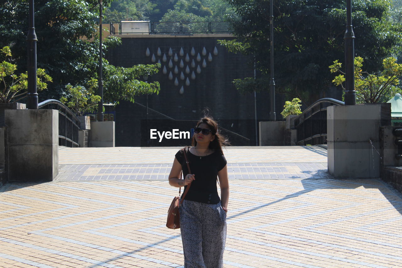 Young woman carrying purse standing on footpath in city