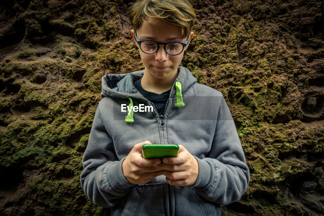 Smiling boy using mobile phone against rock