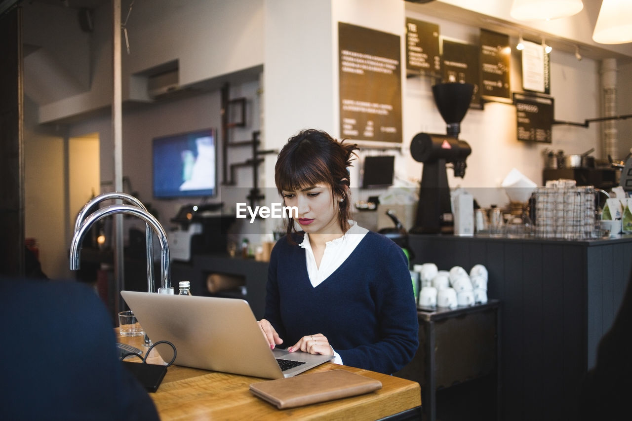 Confident female entrepreneur using laptop sitting at table in office