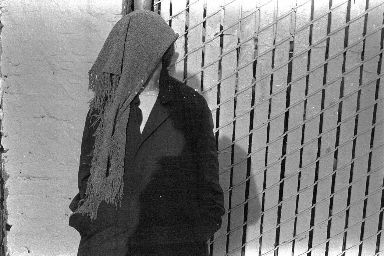 Man face covered with scarf standing against wall