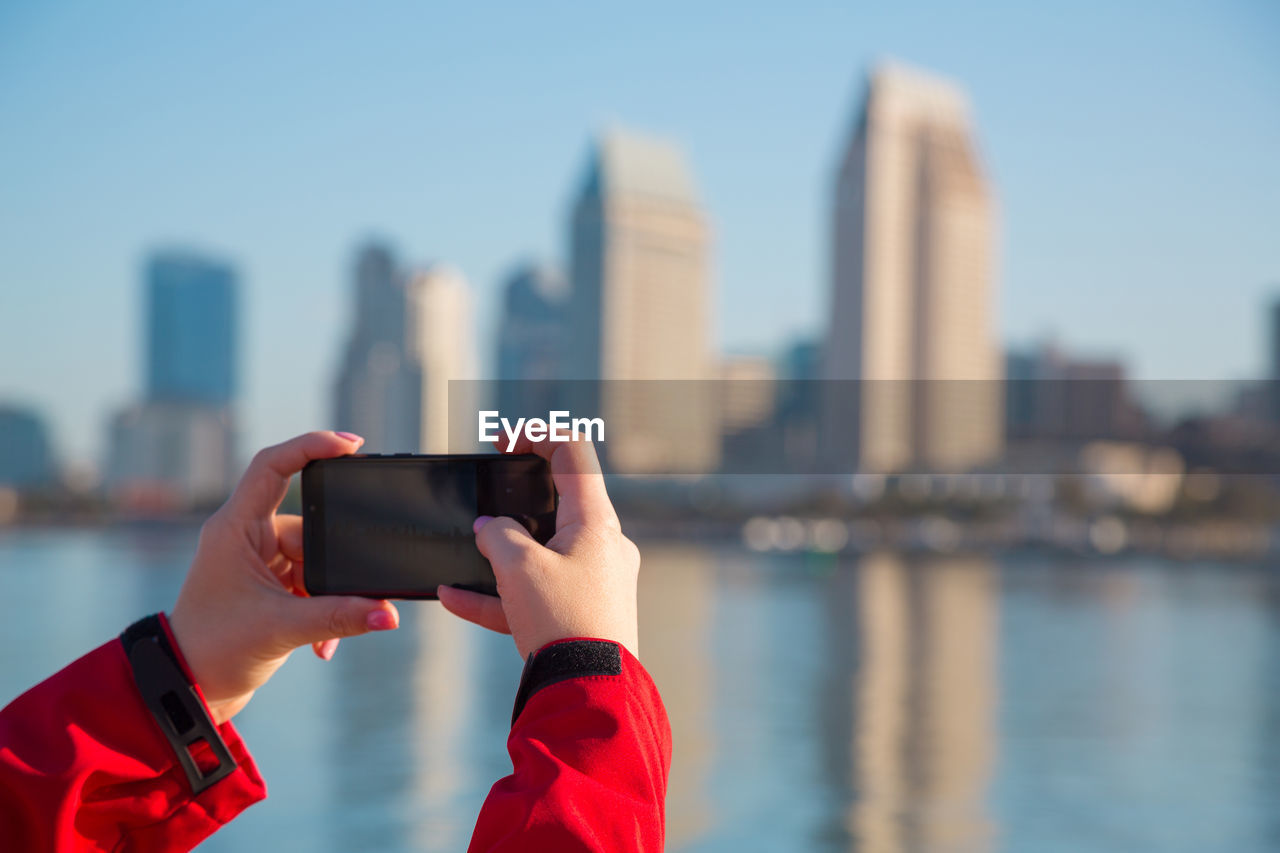 Female hands hold a mobile phone. girl is taking pictures of san diego downtown on her mobile phone