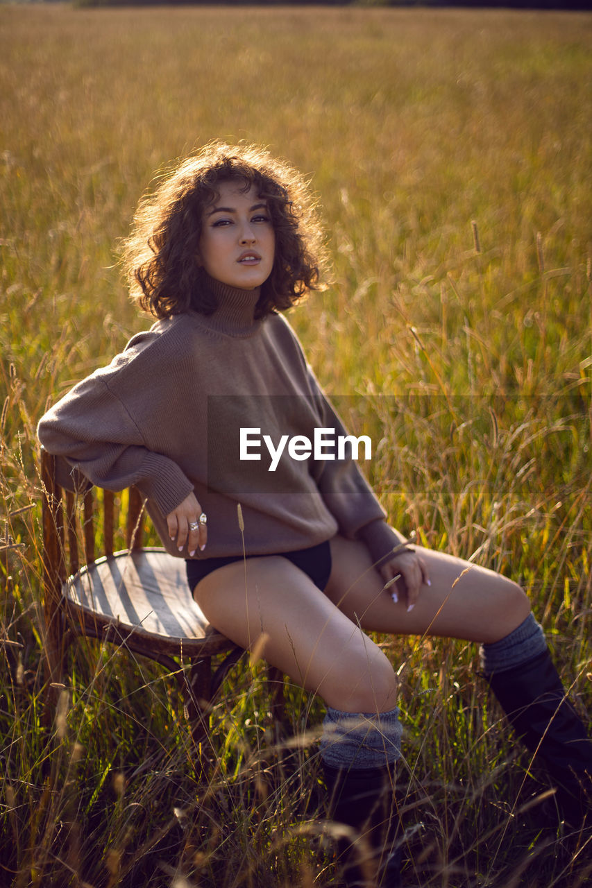  portrait  woman in a sweater and shorts sitting on a field on a wood vintage chair in autumn