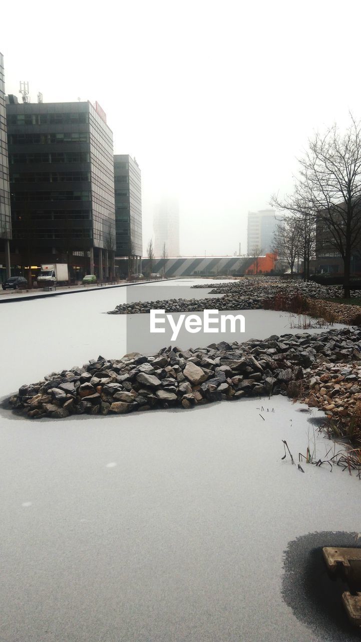 FROZEN RIVER BY BUILDINGS AGAINST SKY IN WINTER