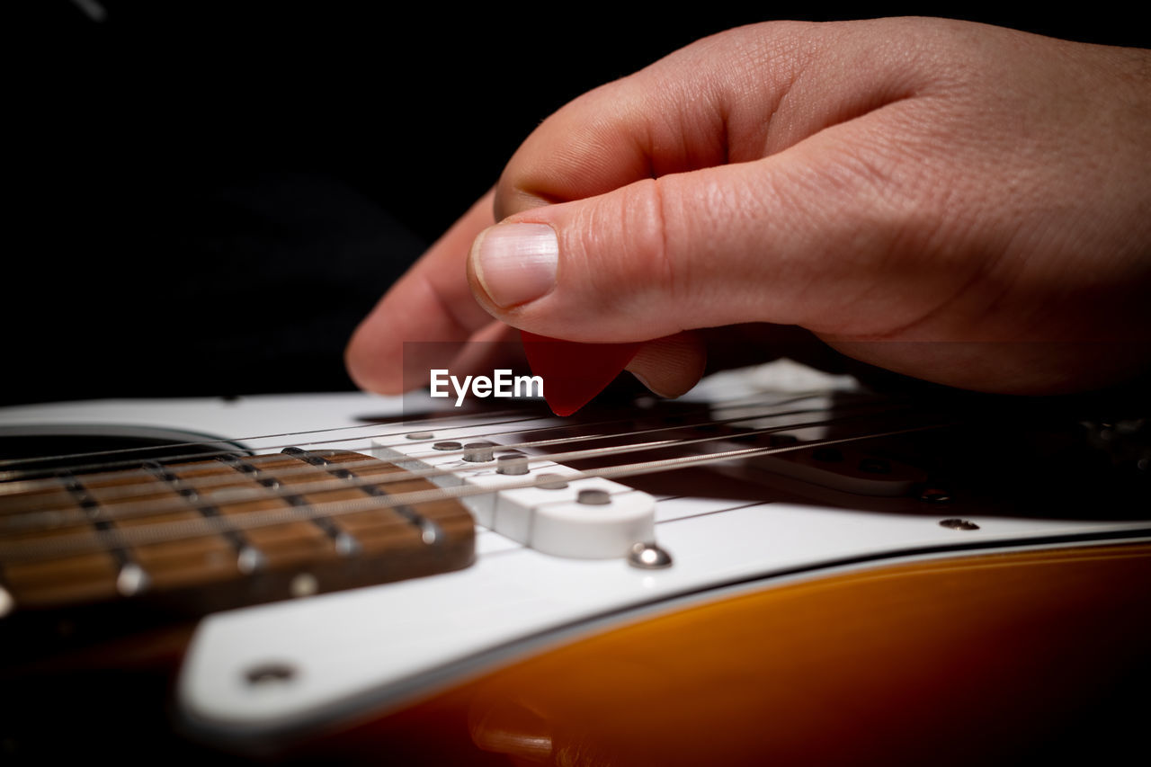 CLOSE-UP OF HAND PLAYING GUITAR IN BLACK BACKGROUND