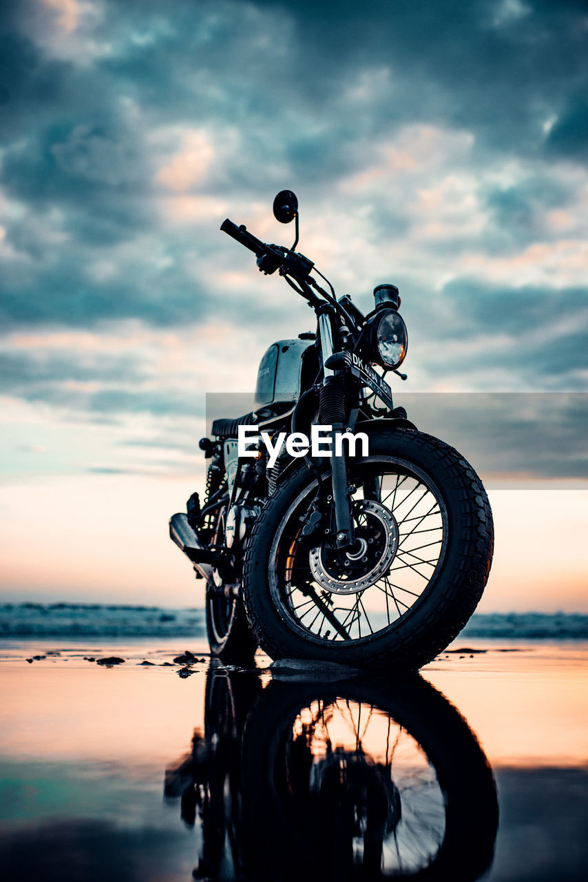 Surface level view of motorcycle at beach against sky during sunset