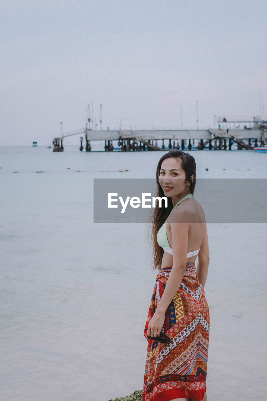 Portrait of woman standing at beach against clear sky