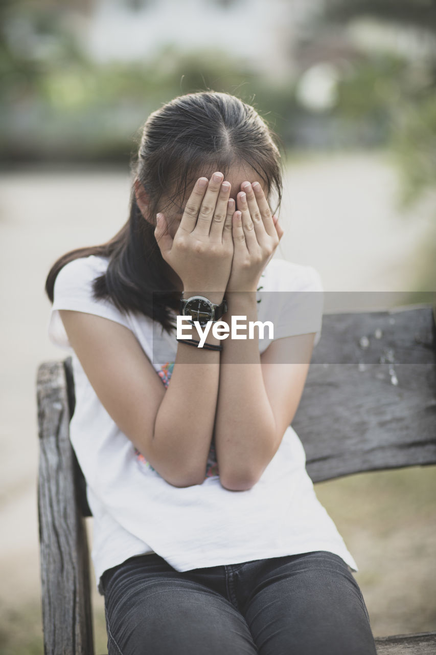 Smiling girl covering face while sitting outdoors