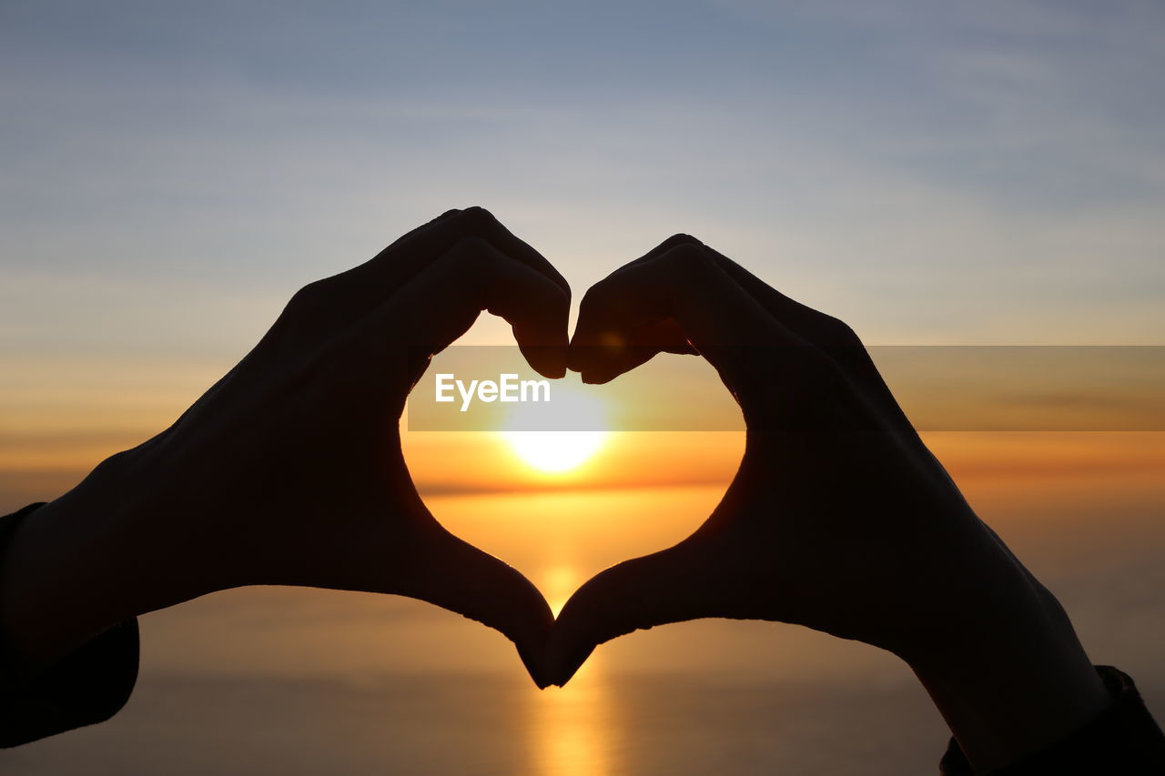 Cropped image of silhouette hands forming heart against sea during sunset