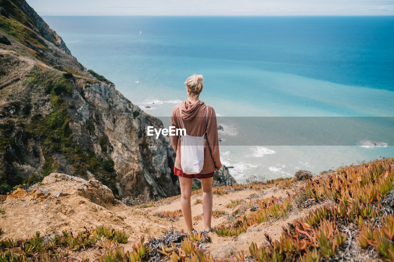 Rear view of woman standing on mountain against sea