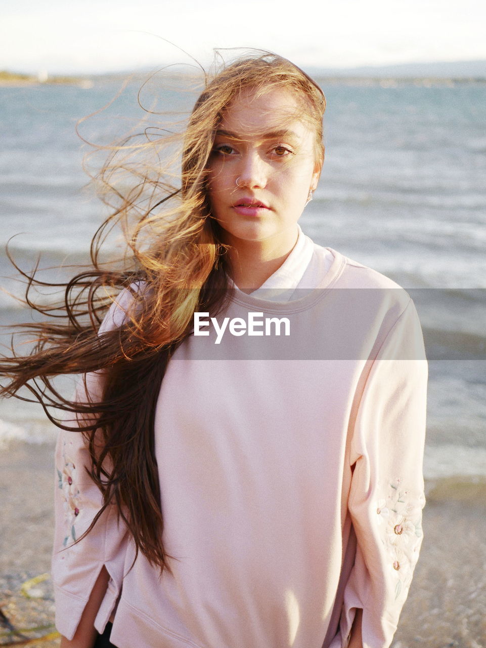 Portrait of beautiful young woman with tousled hair standing at beach