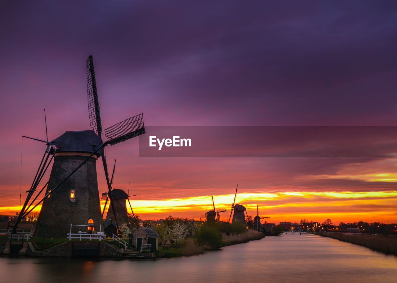 Traditional windmills by river against cloudy sky at kinderdijk