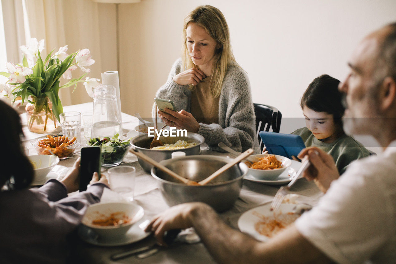 Family using gadgets while sitting at dining table