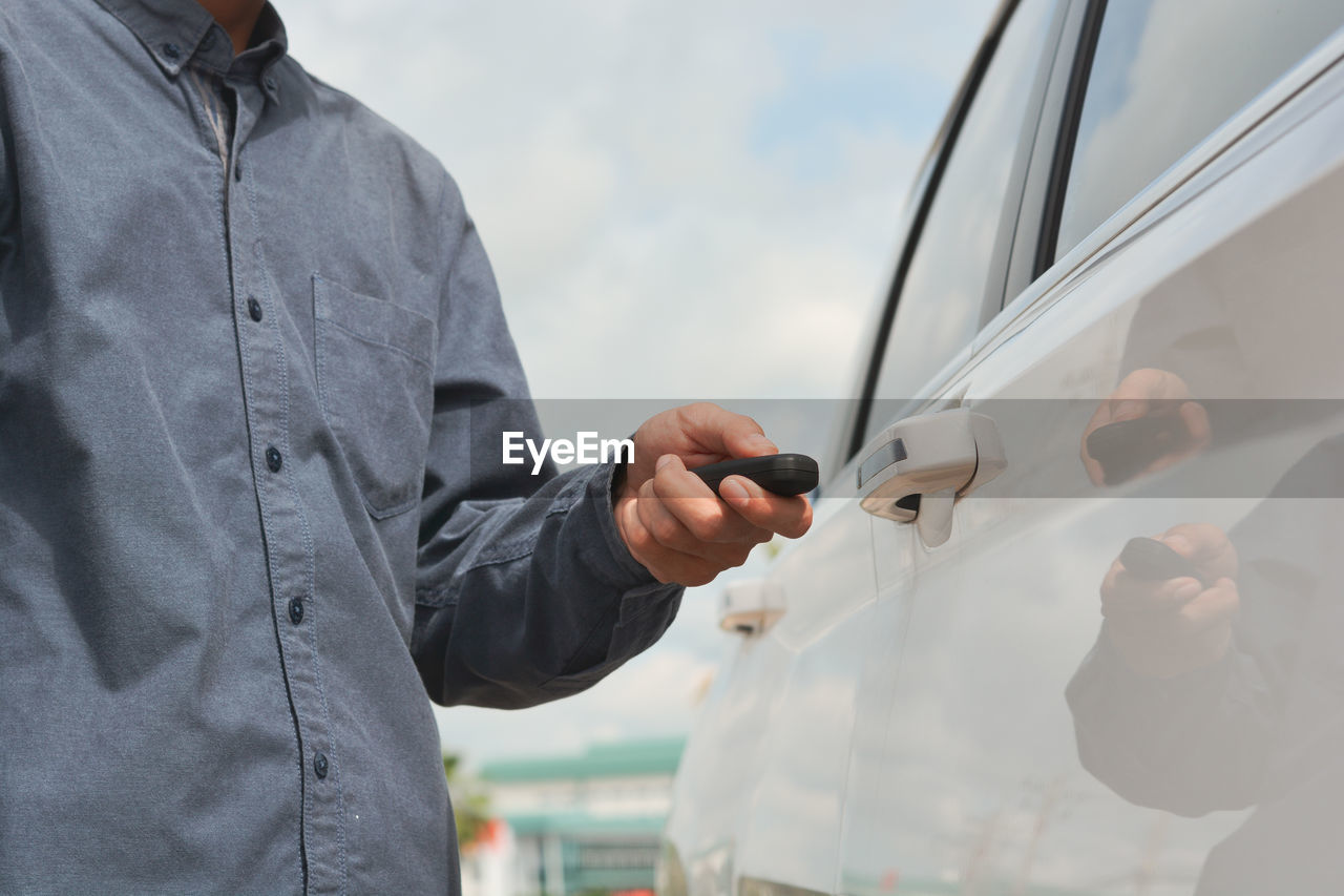 MAN HOLDING MOBILE PHONE WHILE STANDING ON CAR