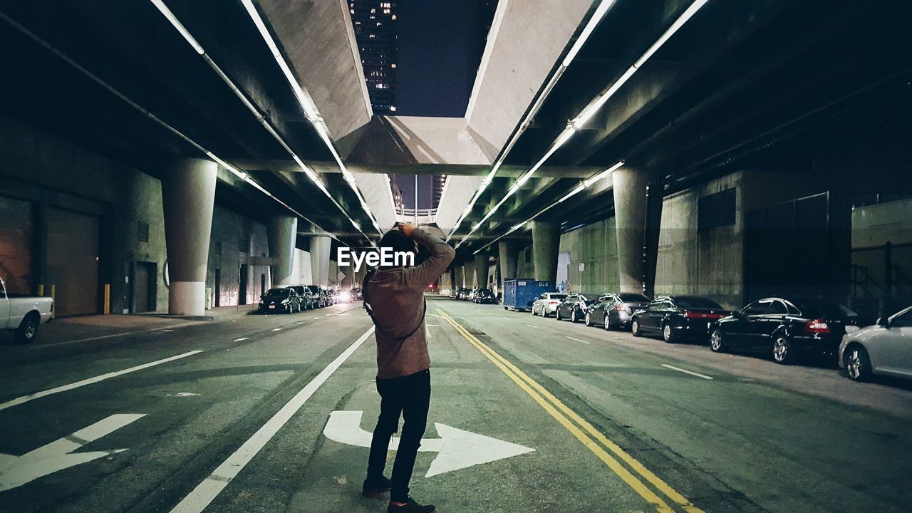 Full length rear view of photographer photographing bridge at night