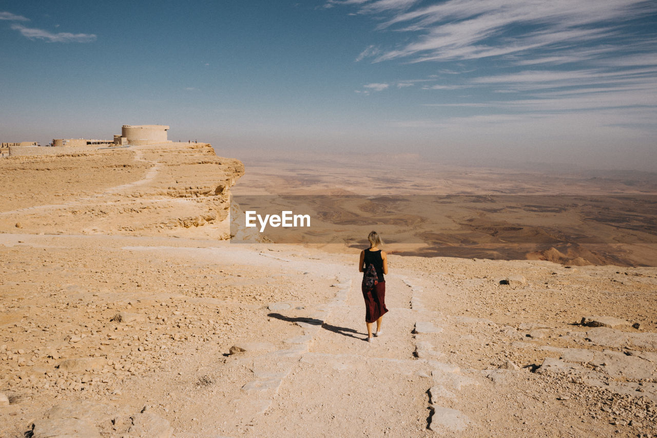 Rear view of woman walking on sand in desert against sky