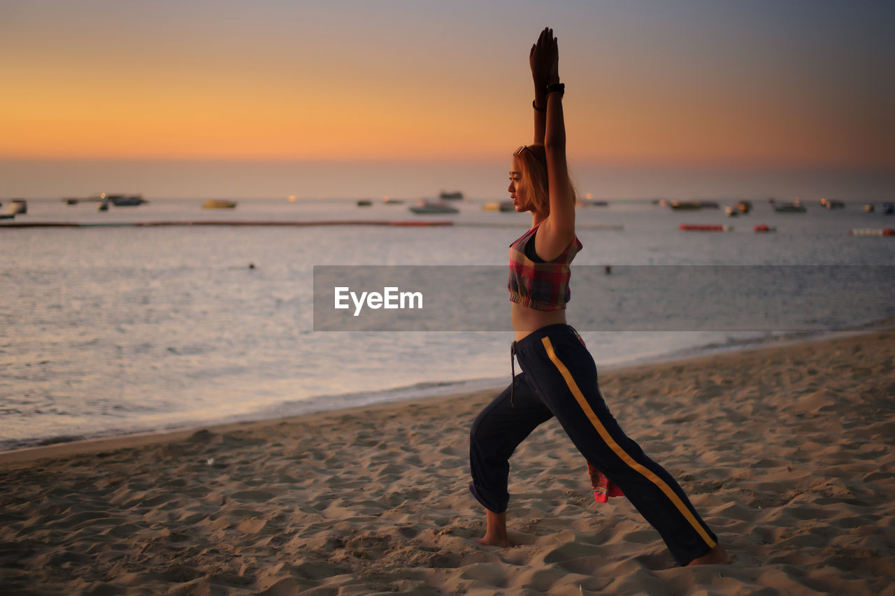 Full length of woman exercising at beach during sunset