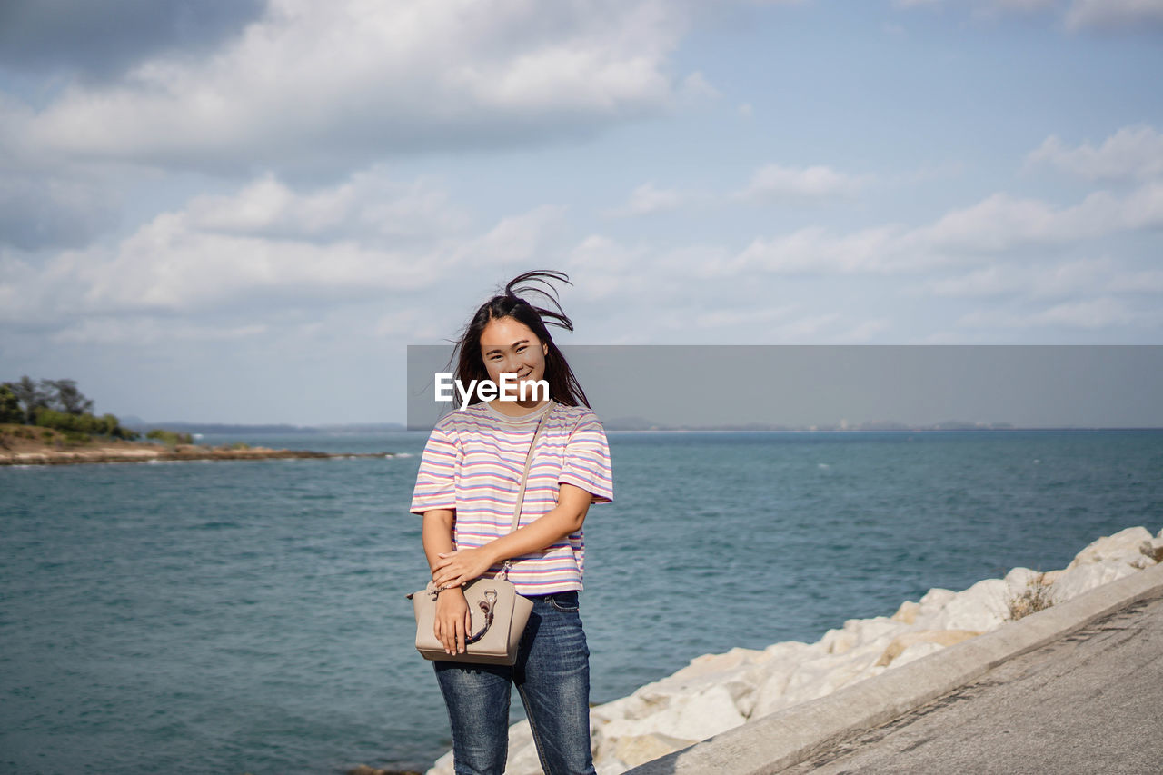 Portrait of smiling woman standing by sea against sky